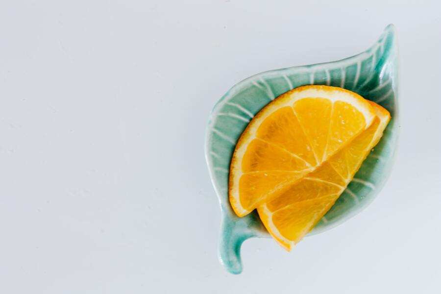 Un pequeño plato verde en forma de hoja contiene varias rodajas de naranja dispuestas en abanico sobre un fondo blanco liso, como invitándole a reclamar la legítima parte de este vibrante manjar.