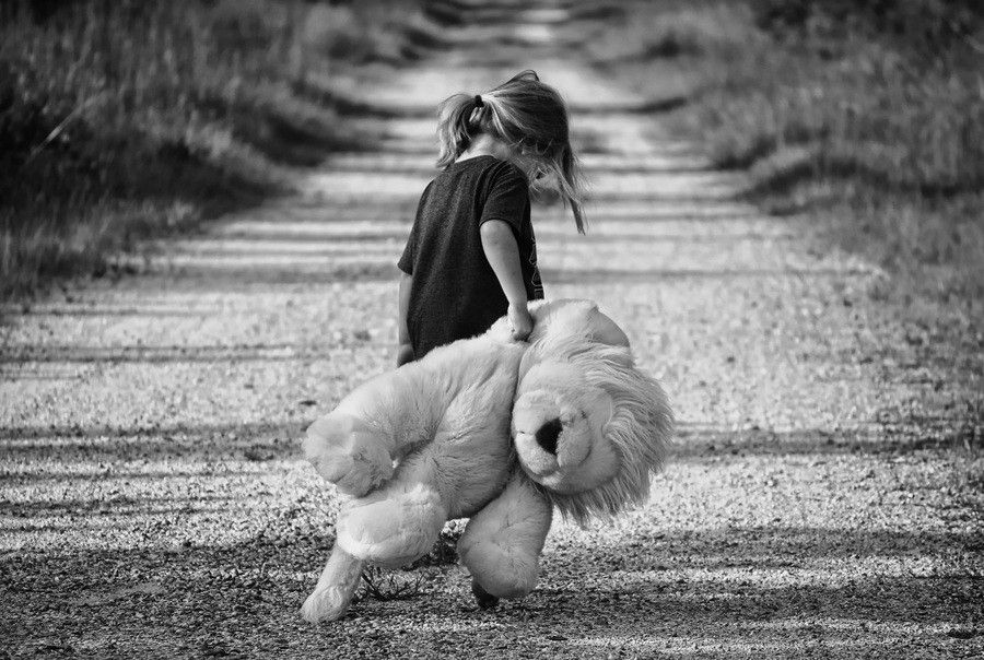 Un niño pequeño camina por un camino de grava con un gran animal de peluche en la mano. La imagen en blanco y negro evoca sutilmente sentimientos relacionados con el síndrome de alienación parental, ya que el niño mira en dirección contraria a la cámara, rodeado de árboles y hierba a ambos lados. Un niño pequeño camina por un camino de grava con un gran animal de peluche en la mano. La imagen en blanco y negro evoca sutilmente sentimientos relacionados con el síndrome de alienación parental, ya que el niño mira en dirección contraria a la cámara, rodeado de árboles y hierba a ambos lados.
